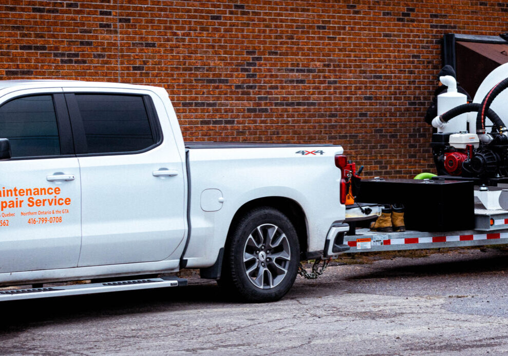 The image is of a white truck with a trailer, specifically a hydrovac unit. The truck is parked and there are details related to maintenance and repair services displayed on the side of the vehicle.